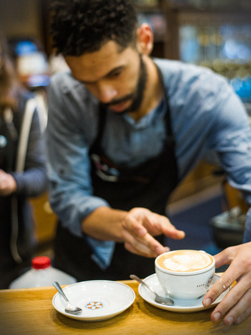 a barista places a beautifully poured latte onto a saucer