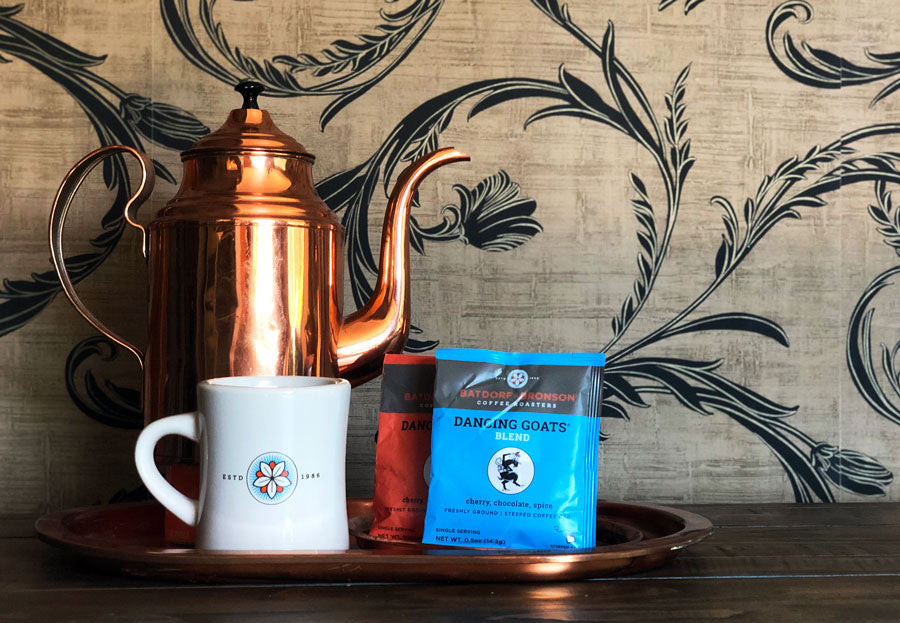 A tray holds a copper kettle, coffee mug, and two packages of Dancing Goats Steeped Coffee