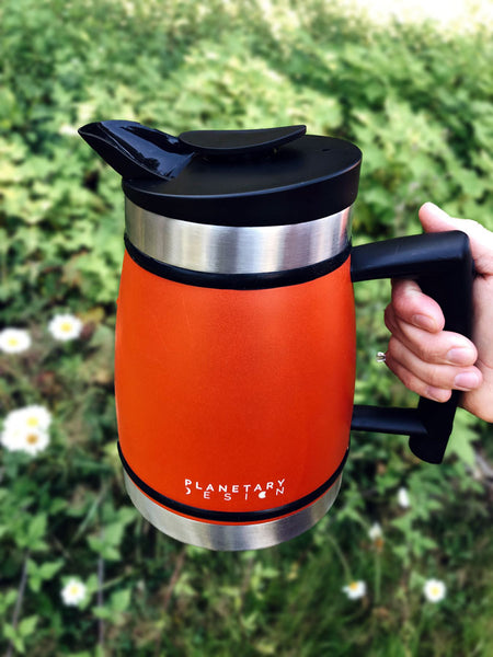 A hand holds the Planetary Design French Press in the air above a field of daisies.