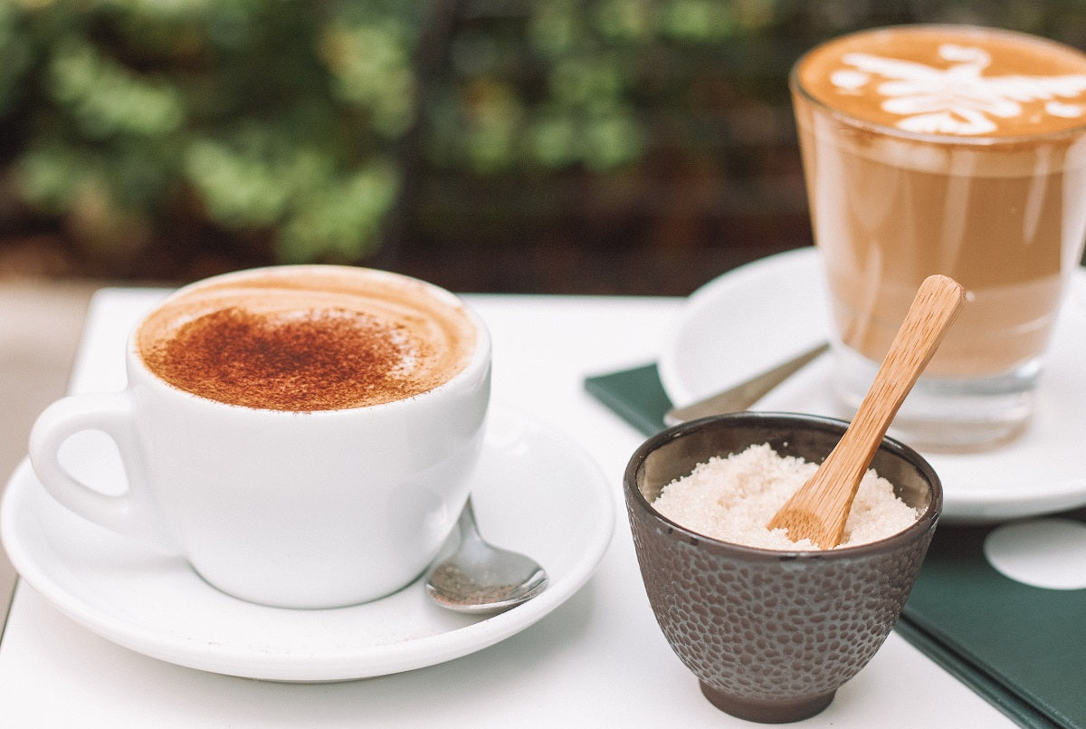 a latte with cinnamon powder on it and a bowl of sugar next to it