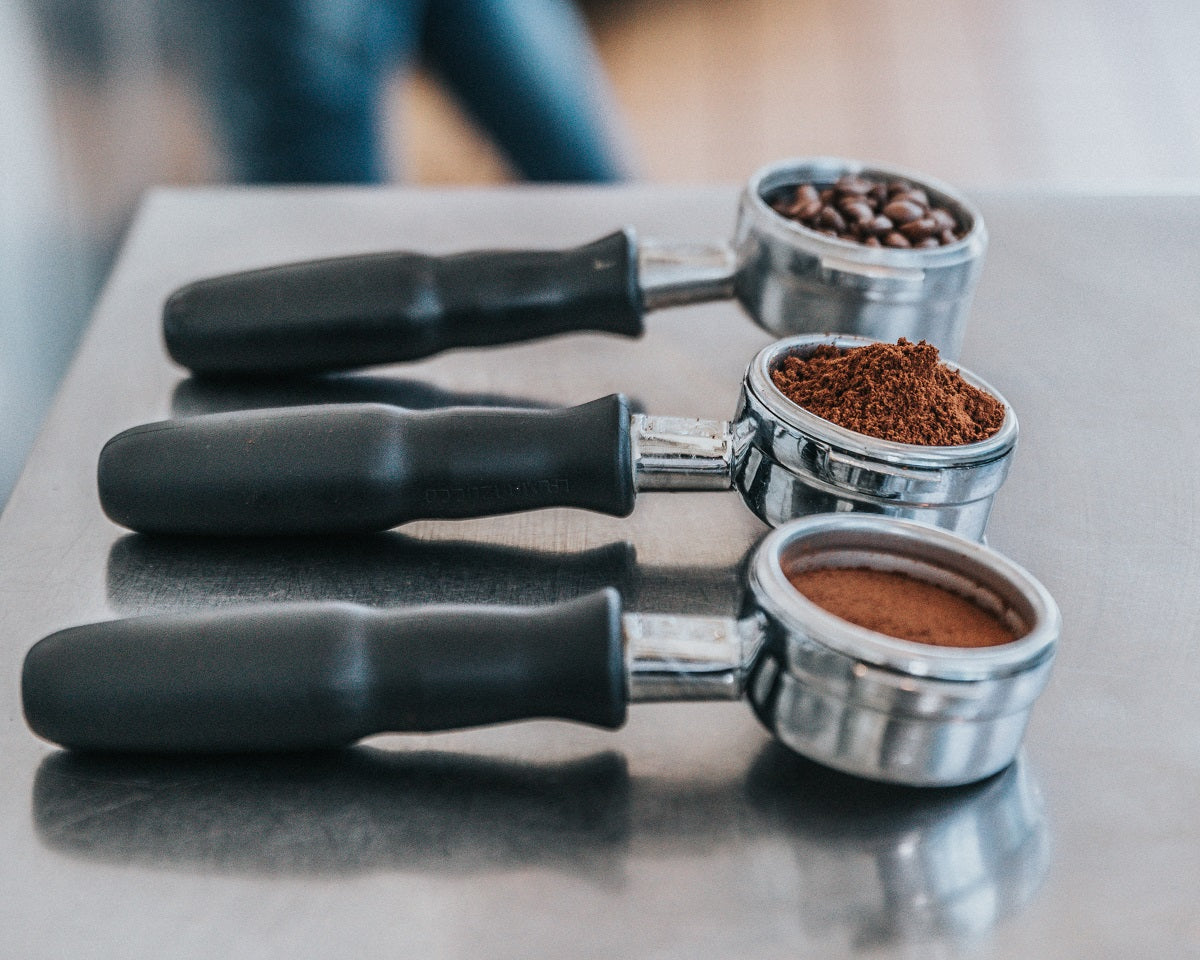 three portafilters filled with coffee beans, ground coffee, tamped coffee