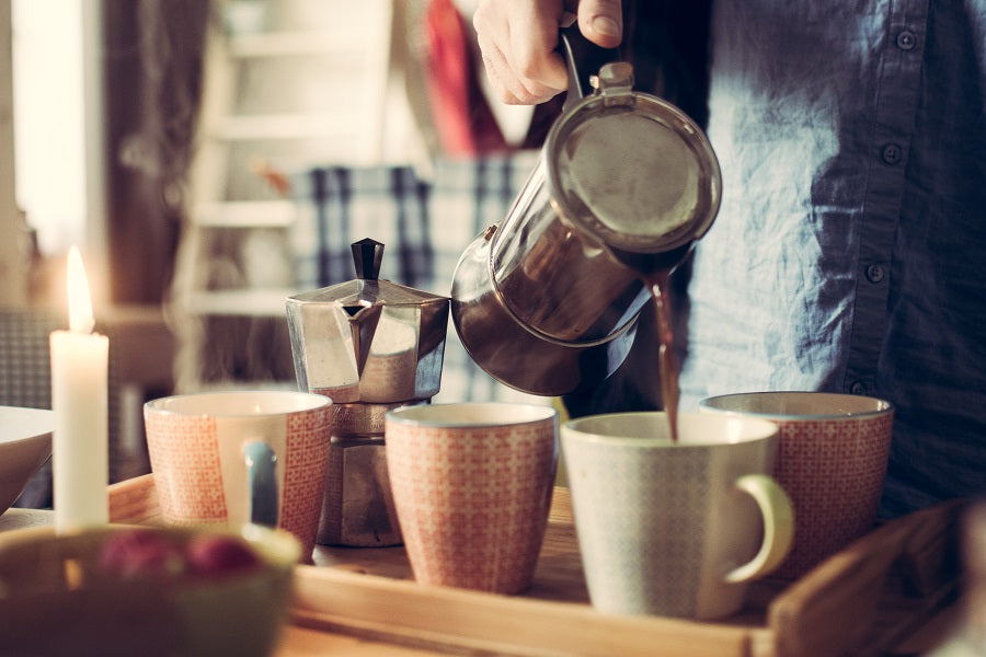 French Press pouring coffee into one of several mugs on a tray