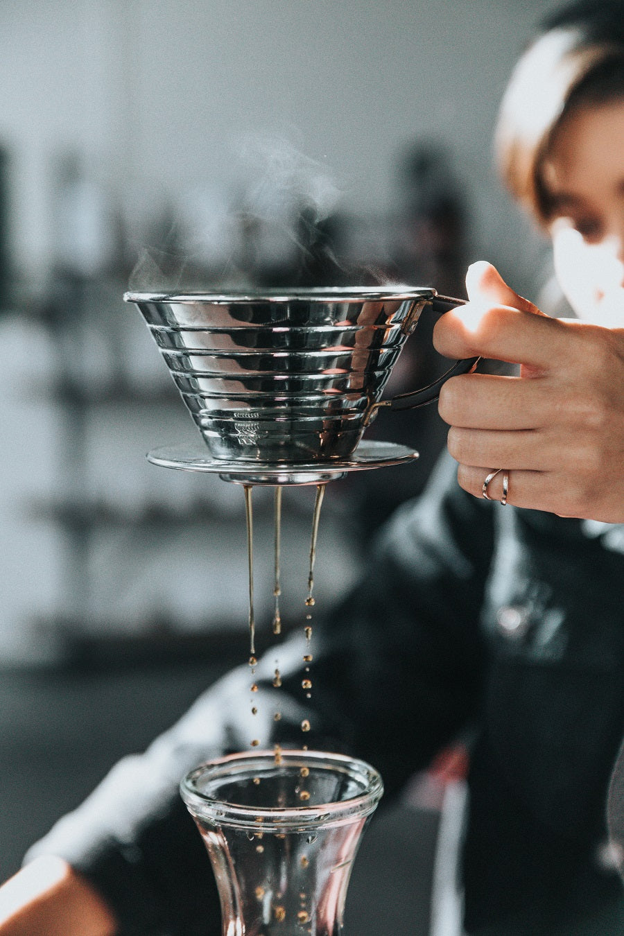 steam coming out of a stainless steel pour over that is brewing coffee into a glass carafe