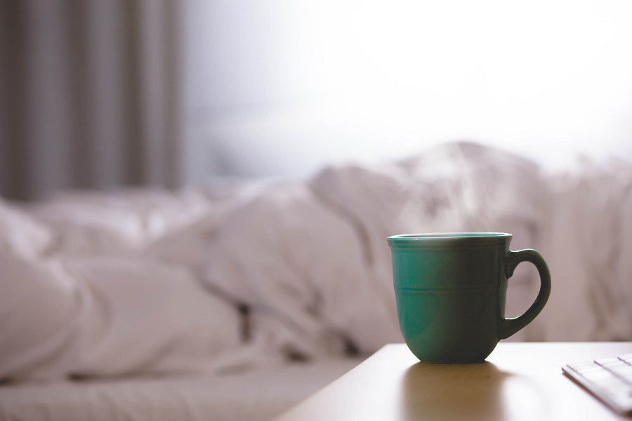 steaming blue mug on side table with white bedding in background 