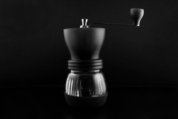 a Hario Skerton manual burr grinder stands against a dark backdrop