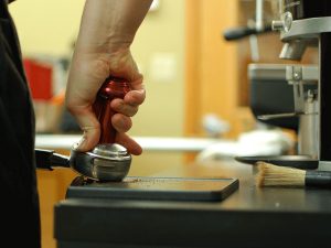 low-angle side view of a tamper being used to compress the coffee in a portafilter