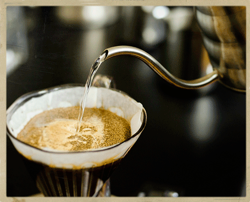 A gooseneck kettle pours hot water over coffee grounds in a clever dripper coffee maker.